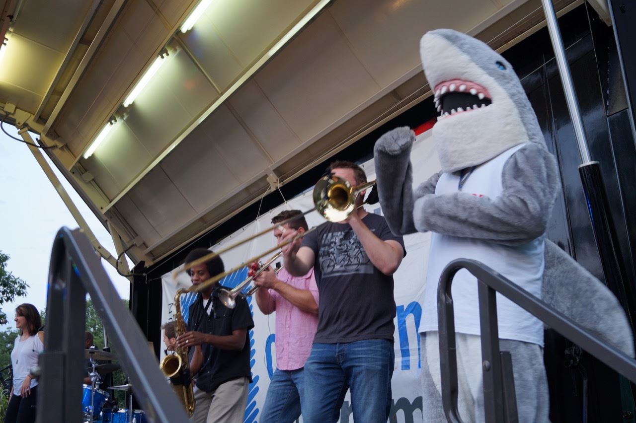 Shark mascot plays the air trombone with members of the band.